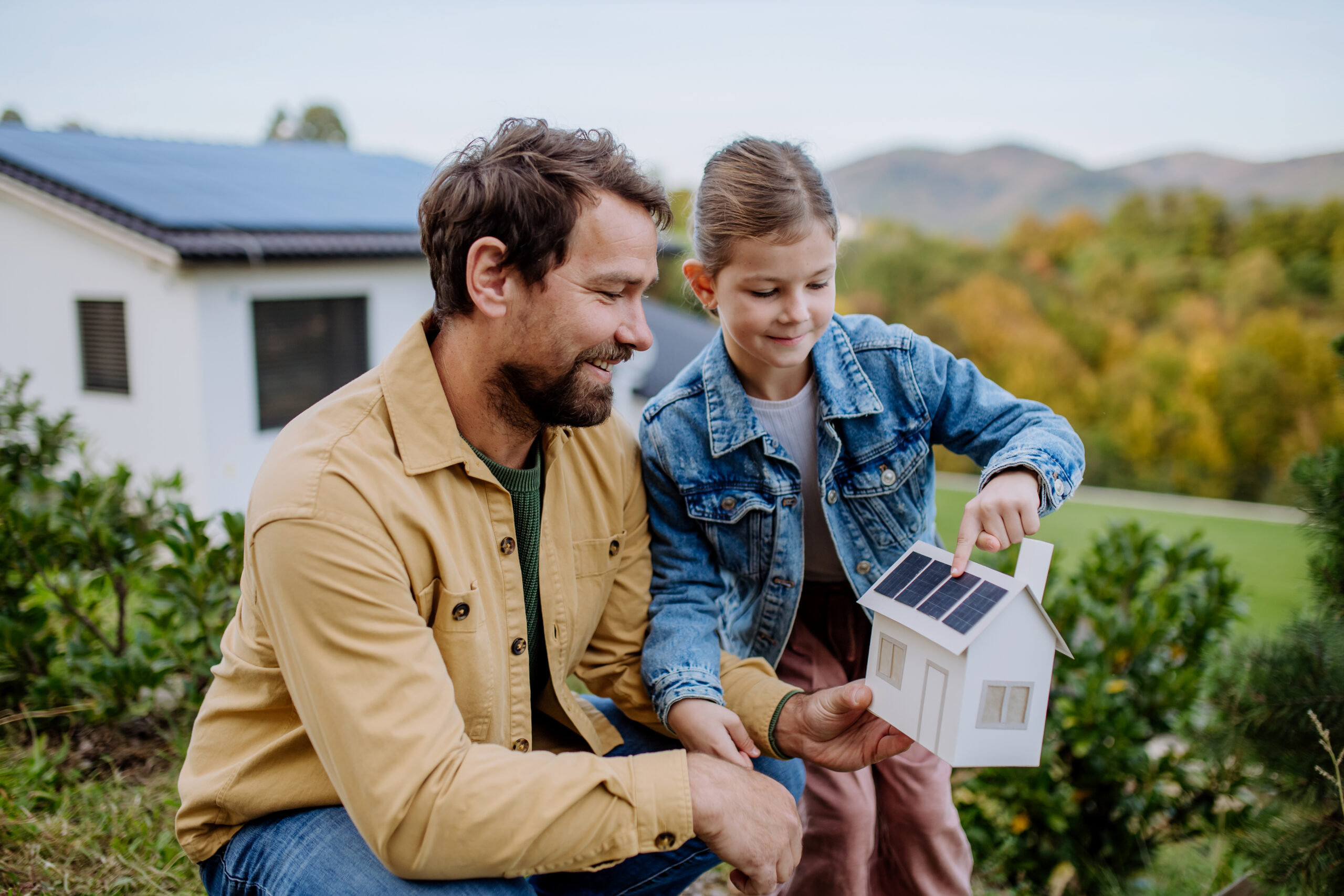 Little girl with her dad holding paper model of house with solar panels, explaining how it works.Alternative energy, saving resources and sustainable lifestyle concept
